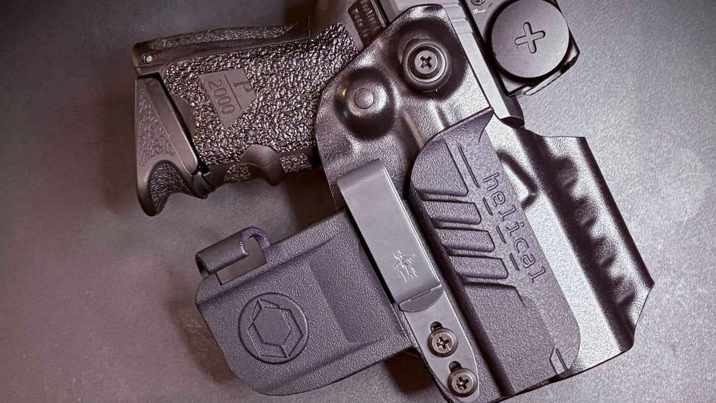 A black Kydex belt carrier holster containing a handgun, shown with a gold webbing belt on a dark gray background.